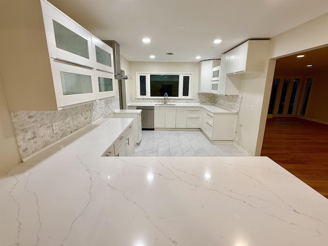 kitchen with decorative backsplash, light stone counters, a sink, white cabinetry, and stainless steel dishwasher