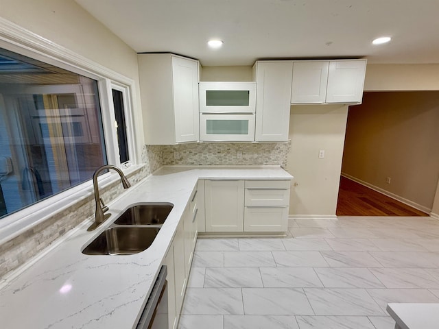 kitchen featuring light stone counters, a sink, white cabinetry, marble finish floor, and backsplash