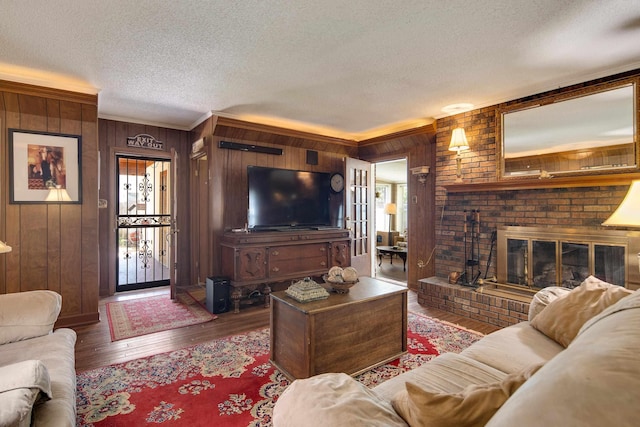 living room with wood-type flooring, ornamental molding, a brick fireplace, wood walls, and a textured ceiling