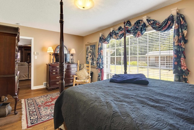 bedroom featuring a textured ceiling, wood finished floors, visible vents, and baseboards