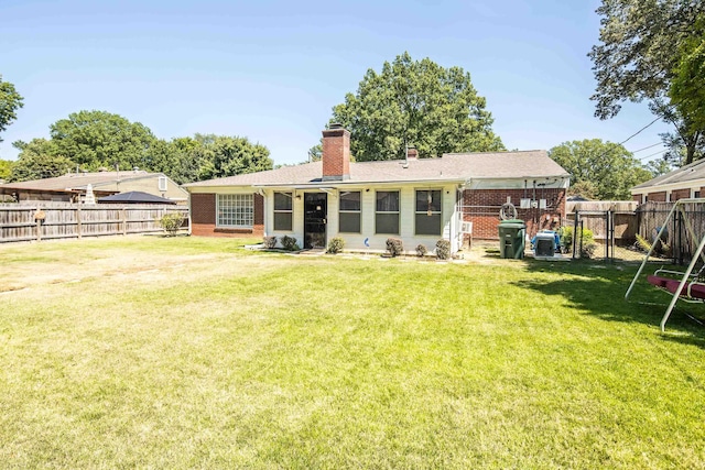 back of property with a chimney, brick siding, a yard, and a fenced backyard