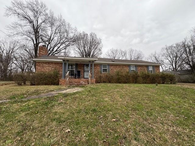 ranch-style home featuring a front yard, covered porch, brick siding, and a chimney