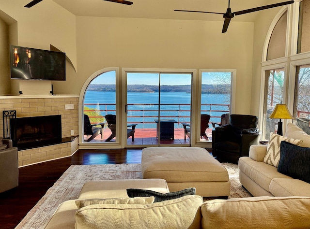 living room featuring a ceiling fan, a fireplace, a towering ceiling, and wood finished floors