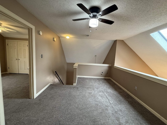 bonus room with a textured ceiling, vaulted ceiling with skylight, carpet floors, visible vents, and baseboards