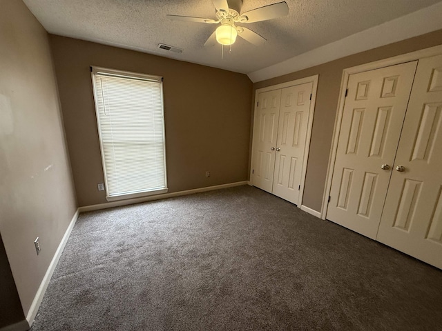 unfurnished bedroom with a textured ceiling, carpet, two closets, and visible vents