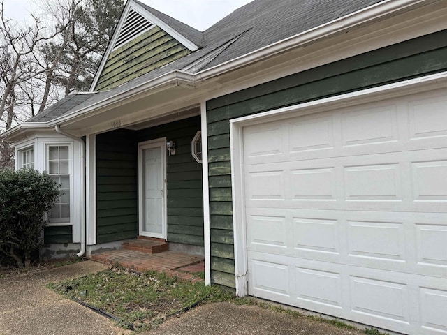 entrance to property featuring a garage and a shingled roof