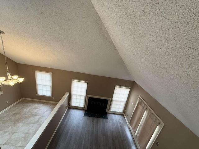 unfurnished living room featuring a chandelier, lofted ceiling, a fireplace, wood finished floors, and baseboards