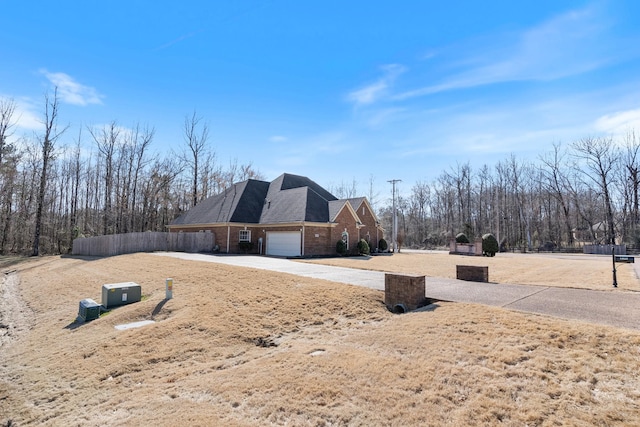 view of property exterior with a garage, driveway, brick siding, and fence