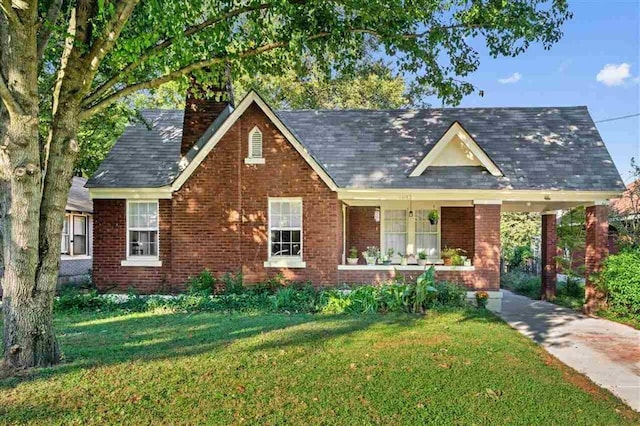 view of front of house featuring a porch, brick siding, a chimney, and a front yard