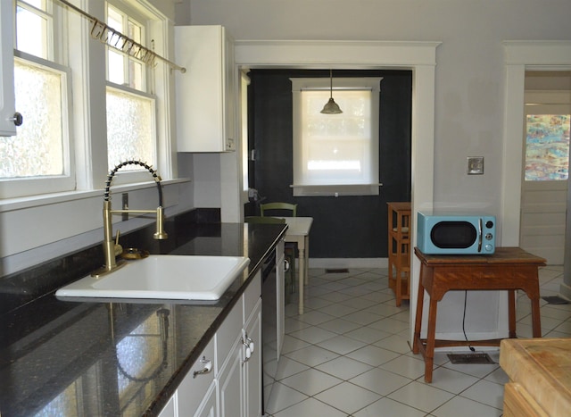 kitchen with light tile patterned floors, dishwashing machine, a sink, white cabinetry, and baseboards