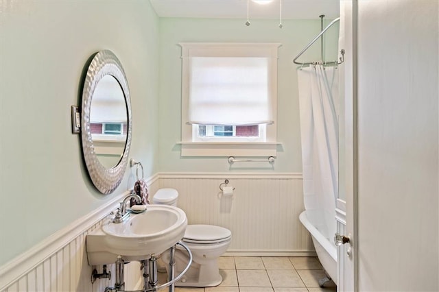 bathroom with toilet, shower / bath combo with shower curtain, wainscoting, a sink, and tile patterned floors