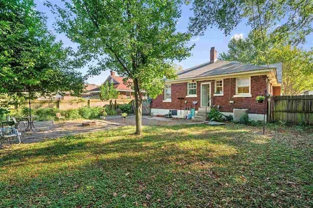 view of front of house featuring entry steps, brick siding, fence, a chimney, and a front yard