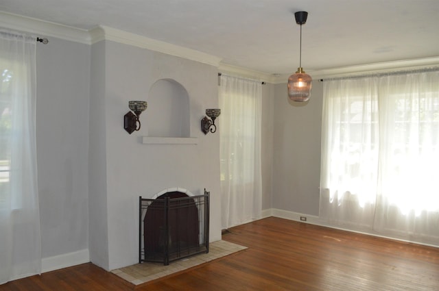 unfurnished dining area featuring ornamental molding, baseboards, a fireplace with flush hearth, and wood finished floors