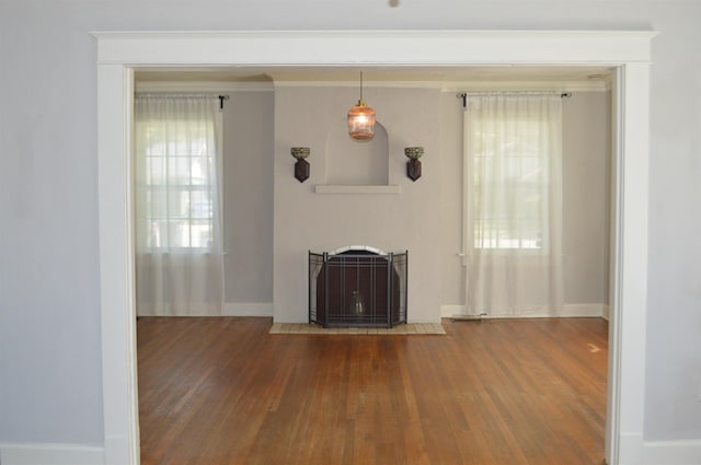 unfurnished living room with a fireplace with flush hearth, baseboards, ornamental molding, and hardwood / wood-style floors