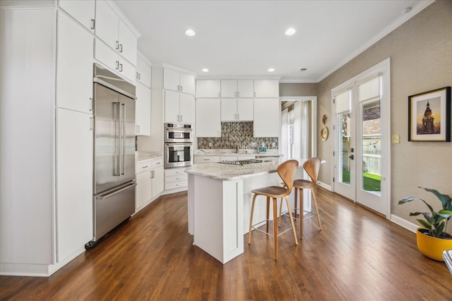 kitchen with white cabinets, decorative backsplash, dark wood-style floors, appliances with stainless steel finishes, and a kitchen bar