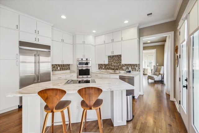 kitchen featuring dark wood-style floors, stainless steel appliances, decorative backsplash, ornamental molding, and a kitchen breakfast bar