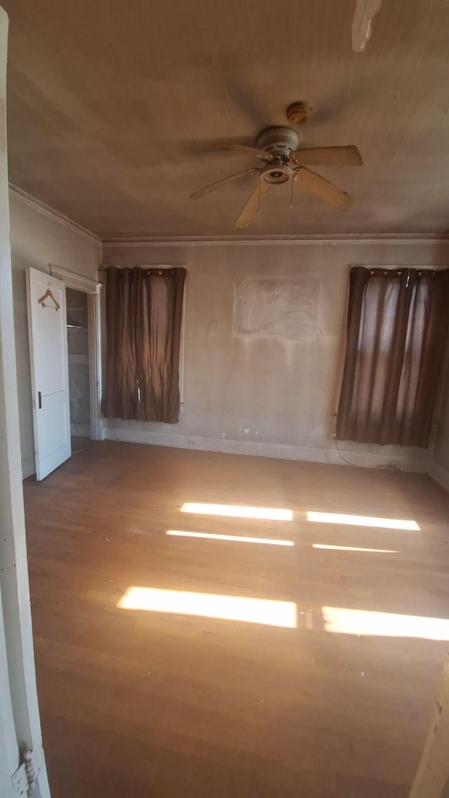 empty room featuring ceiling fan, crown molding, and wood finished floors