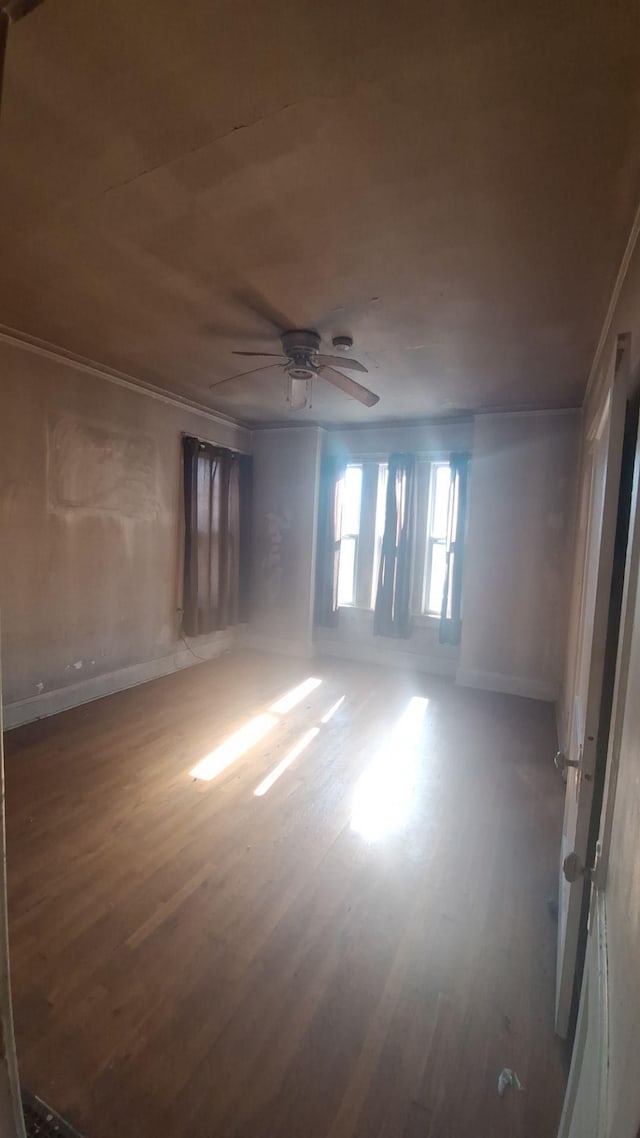 empty room featuring baseboards, ceiling fan, wood finished floors, and crown molding