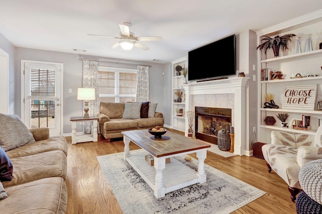 living room featuring a tiled fireplace, a healthy amount of sunlight, and light wood-type flooring