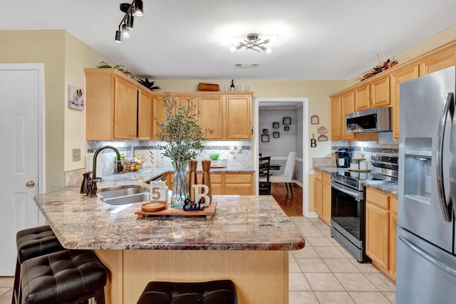 kitchen with appliances with stainless steel finishes, a peninsula, and light brown cabinetry