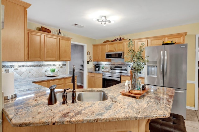 kitchen featuring light brown cabinets, light stone counters, decorative backsplash, appliances with stainless steel finishes, and a sink