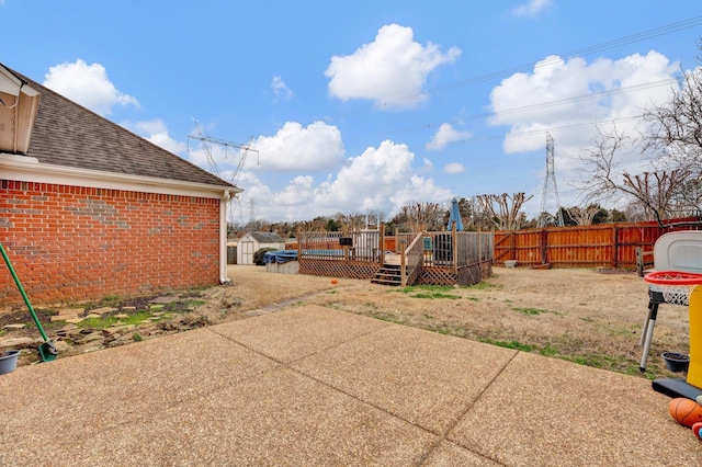 view of yard featuring a wooden deck, a fenced backyard, a patio area, a storage unit, and an outbuilding