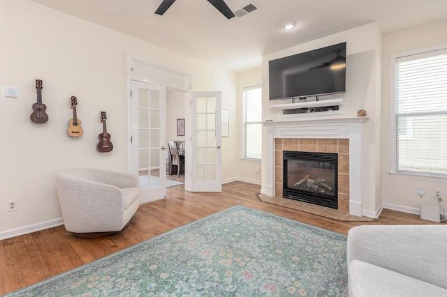 living area featuring french doors, a fireplace, visible vents, wood finished floors, and baseboards