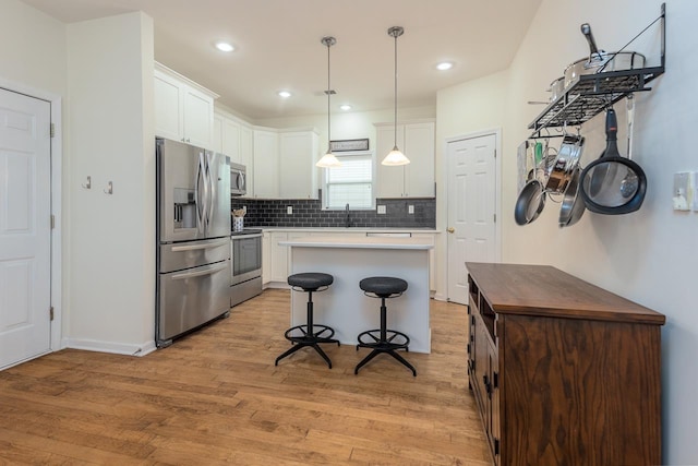 kitchen featuring light wood finished floors, a breakfast bar area, appliances with stainless steel finishes, white cabinetry, and backsplash