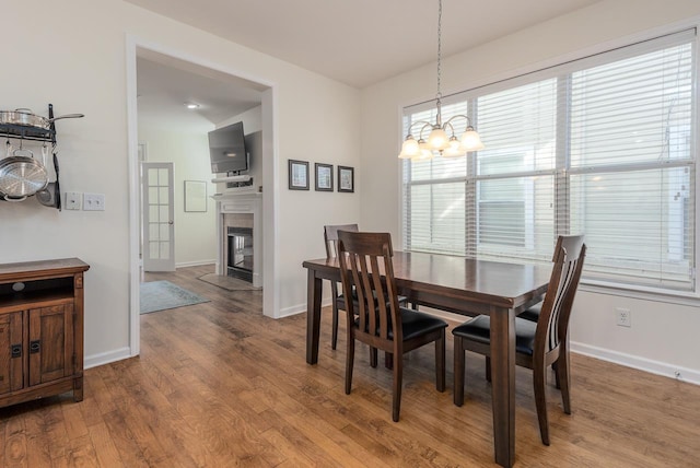 dining room featuring a tile fireplace, an inviting chandelier, baseboards, and wood finished floors