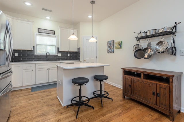 kitchen featuring tasteful backsplash, stainless steel fridge, a kitchen island, light countertops, and white cabinetry