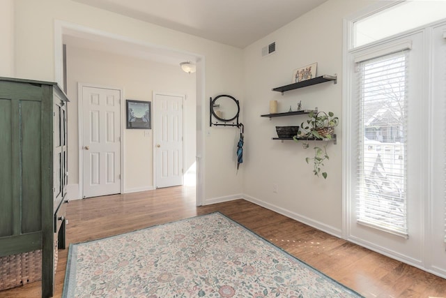 foyer entrance with baseboards, visible vents, and wood finished floors