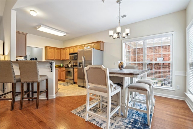 dining area featuring light wood finished floors, baseboards, visible vents, and a chandelier