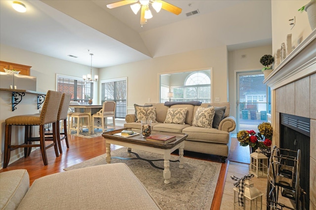 living area featuring ceiling fan with notable chandelier, light wood-style flooring, a tile fireplace, and visible vents