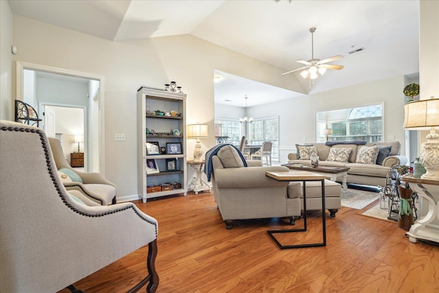 living room featuring light wood-type flooring, visible vents, vaulted ceiling, and ceiling fan with notable chandelier