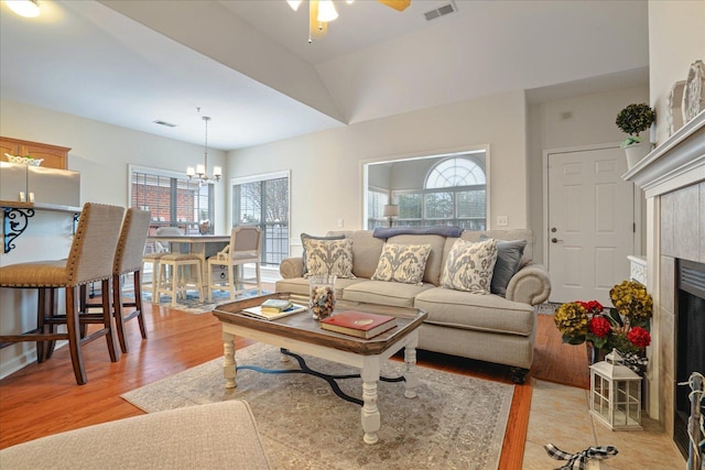 living room with a tile fireplace, visible vents, light wood-style flooring, and ceiling fan with notable chandelier