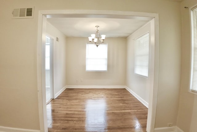 spare room with a chandelier, wood finished floors, visible vents, and baseboards