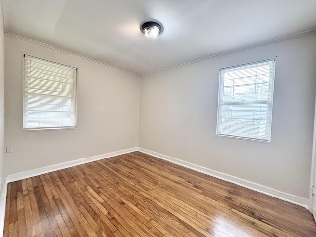 empty room featuring wood-type flooring, baseboards, and crown molding