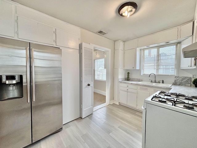 kitchen with a sink, visible vents, light countertops, stainless steel refrigerator with ice dispenser, and white gas range