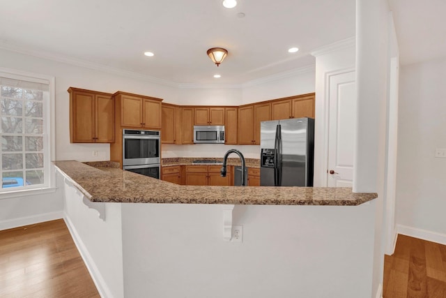 kitchen featuring baseboards, brown cabinetry, a breakfast bar area, stainless steel appliances, and light wood-type flooring