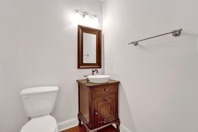 half bath featuring toilet, wood finished floors, vanity, and baseboards