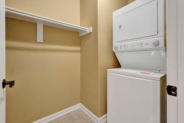 clothes washing area featuring baseboards, laundry area, light tile patterned floors, and stacked washer / drying machine