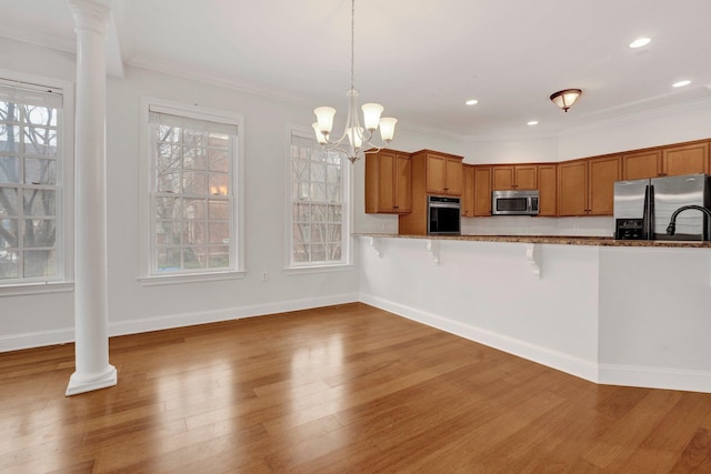 kitchen featuring appliances with stainless steel finishes, brown cabinetry, wood finished floors, and decorative columns