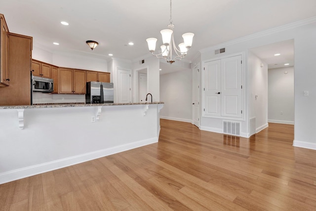 kitchen with appliances with stainless steel finishes, brown cabinetry, visible vents, and a breakfast bar area