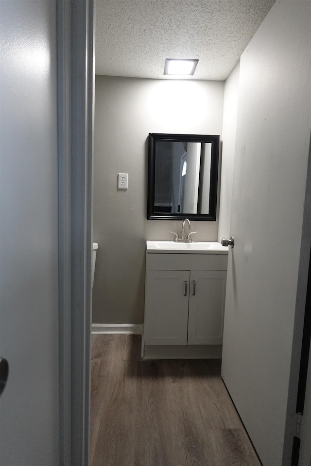 bathroom featuring baseboards, toilet, wood finished floors, a textured ceiling, and vanity