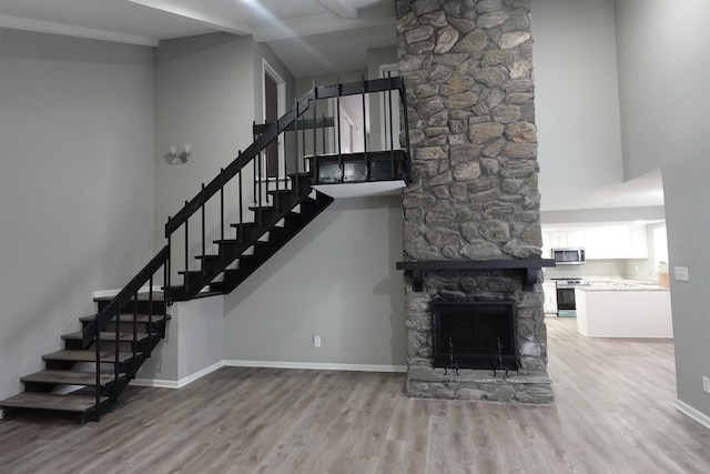 unfurnished living room with a high ceiling, baseboards, wood finished floors, and a stone fireplace