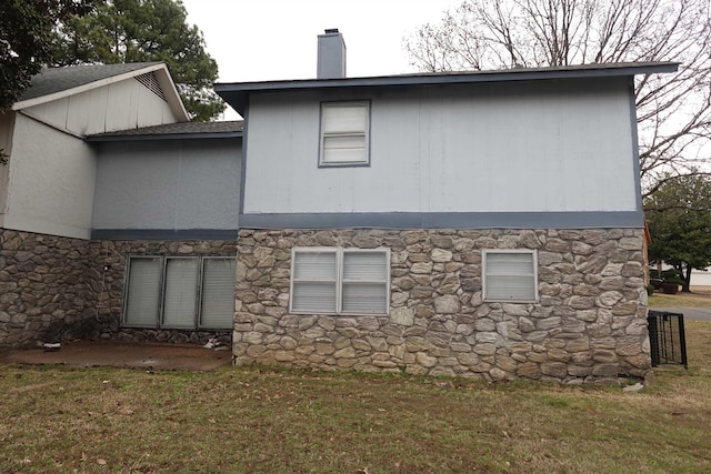 back of house with a shingled roof, a chimney, and a lawn