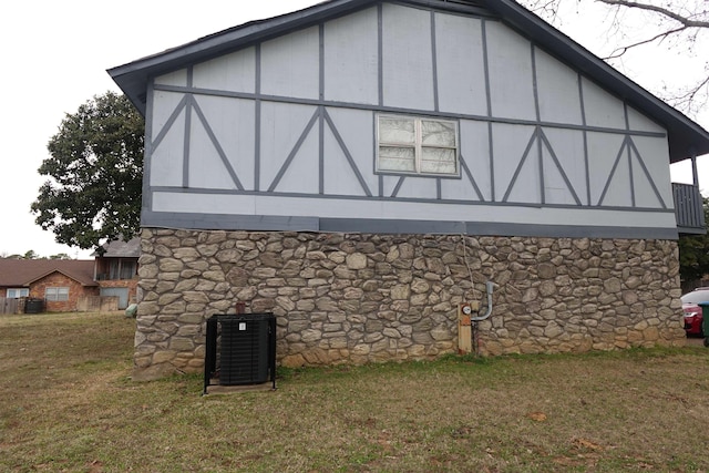 view of property exterior featuring stone siding, central AC, and a lawn