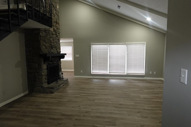 unfurnished living room with high vaulted ceiling, a stone fireplace, wood finished floors, and baseboards