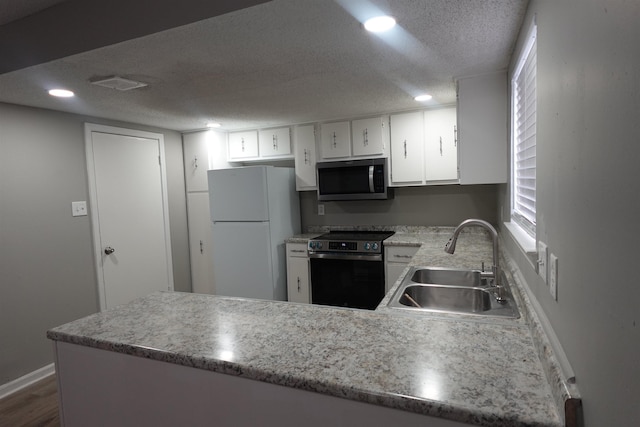 kitchen featuring dark wood-style floors, appliances with stainless steel finishes, a sink, a textured ceiling, and a peninsula