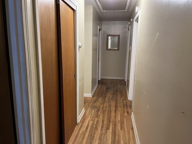 hallway featuring wood finished floors, attic access, and baseboards